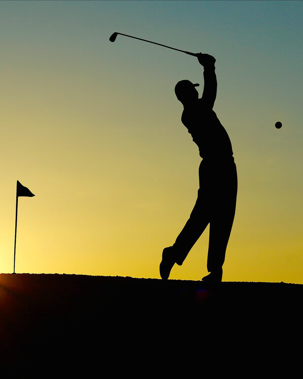 Ein Golfer schwingt seinen Schläger auf einem Golfplatz bei Sonnenuntergang.